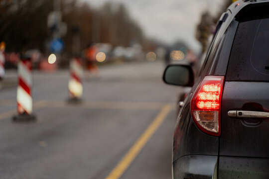 Car waiting at road construction area with red tail lights on and safety barriers ahead representing urban traffic control, transportation safety, and infrastructure maintenance environment