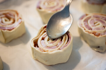 Rolls of bacon on a baking sheet with a metal spoon.