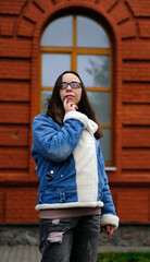 Young Adult in Casual Outfit Standing in Front of Red Brick Building With Large Windows During a...