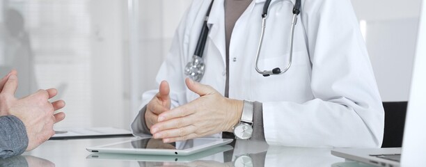 Doctor consulting patient, discussing diagnosis, using digital tablet in modern medical clinic. Medicine and health care