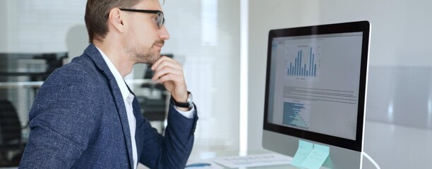 Fototapeta premium Businessman in a blue jacket analyzing financial data charts on computer, making important business decisions in modern office. Business people concept