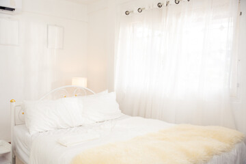 Bright cozy bedroom with white bedding, fluffy blanket, and sheer curtains lit by natural light....