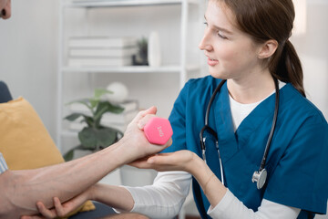 Female nurse assisting elderly man with hand exercise using 1kg dumbbell at home, highlighting rehabilitation, strength training, and senior care therapy in a home healthcare setting.