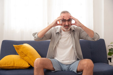 Elderly man suffering from headache or migraine at home, expressing pain, stress, and senior health...