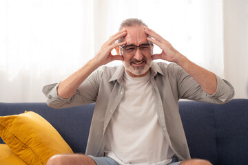 Elderly man suffering from headache or migraine at home, expressing pain, stress, and senior health...
