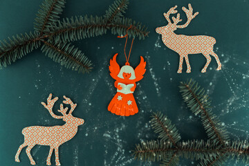 Festive Christmas background with paper angel and reindeer ornaments on dark green surface decorated with fir branches and glitter.