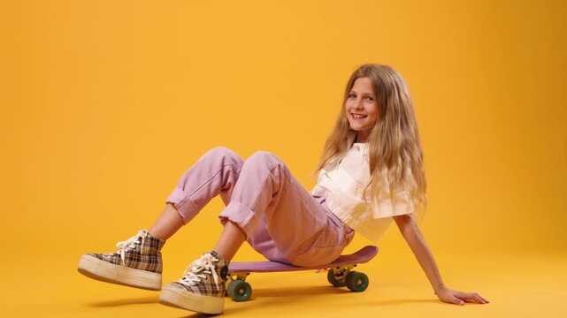 Stylish young girl falling off her skateboard in a studio