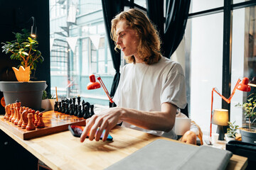 Young man enjoying a chess game in a cozy indoor space with plants