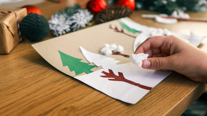 Child's hand adding cotton ball snow to a handmade Christmas card