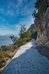 Scenic stone path by rocky coast in Nafplio, Peloponnese, Greece under blue sky