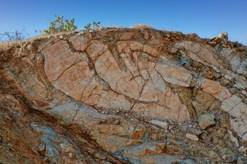 A detailed close-up of a heavily fractured rock face displaying dominant orange and red tones