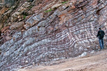A detailed close-up of a layered rock face, showing alternating bands of reddish-brown and...