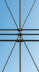 Fototapeta premium Intricate network of thick metal strands forming the main cables of a massive suspension crossing structure against a bright sky background, tension, infrastructure, industrial