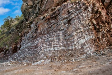 Naklejka premium Layered rock formations of the Zagros Mountains, featuring distinctive red and green sedimentary strata under a clear sky in Kurdistan