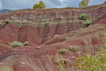 Layered rock formations of the Zagros Mountains, featuring distinctive red and green sedimentary strata under a clear sky in Kurdistan
