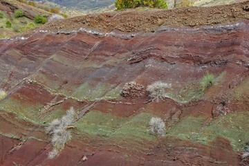 Layered rock formations of the Zagros Mountains, featuring distinctive red and green sedimentary strata under a clear sky in Kurdistan