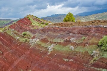 Layered rock formations of the Zagros Mountains, featuring distinctive red and green sedimentary strata under a clear sky in Kurdistan
