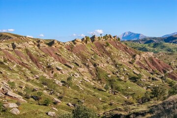 Layered rock formations of the Zagros Mountains, featuring distinctive red and green sedimentary strata under a clear sky in Kurdistan