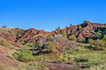 Layered rock formations of the Zagros Mountains, featuring distinctive red and green sedimentary strata under a clear sky in Kurdistan