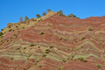 Layered rock formations of the Zagros Mountains, featuring distinctive red and green sedimentary strata under a clear sky in Kurdistan