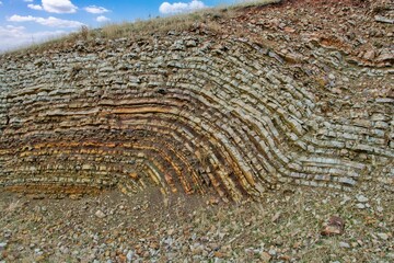 Layered rock formations of the Zagros Mountains, featuring distinctive red and green sedimentary strata under a clear sky in Kurdistan