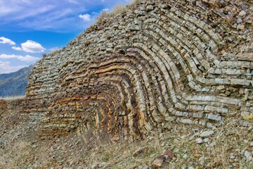 Layered rock formations of the Zagros Mountains, featuring distinctive red and green sedimentary strata under a clear sky in Kurdistan