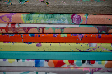 Colorful abstract acrylic paintings on canvas stacked together. Close-up view of textured art pieces with vibrant paint details and creative patterns in an artist’s studio.
