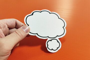 Hand holding blank white speech bubble on orange background