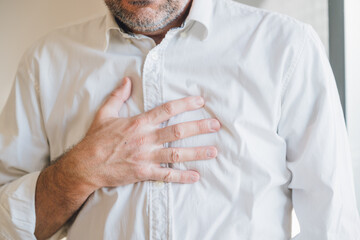 Businessman in white shirt suffering from severe chest pain, close up of man clutching his chest due to sudden heart pain, emergency health concept.