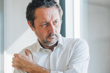 Unshaved mature businessman suffering from severe shoulder pain, holding arm in discomfort.