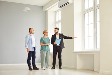 Realtor and agent guide a senior couple through new apartment during a tour and viewing, helping buyers assess the interior and showing key home features. Real estate market and buying property.