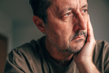 Restless adult man sitting in silence, leaning on hand, showing tired and uneasy facial expression in closeup portrait, procrastination concept.