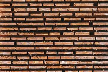 Stack of wooden construction planks arranged for drying. Pile of lumber boards stored outdoors in neat rows.