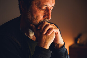 Worried man sitting alone in dark room with warm low key light, serious expression and emotional tension.
