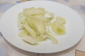 Thin slices of fresh white onion arranged on a plain white plate, ready to be used as a topping or ingredient.