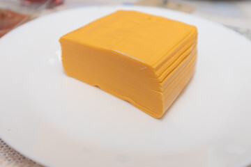 Neatly stacked yellow processed cheese slices placed on a clean white plate, ready for use in sandwiches or burgers.