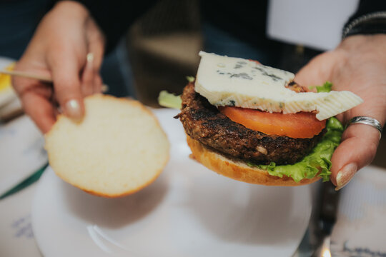 An open-faced burger with a grilled patty, melted cheese, and creamy sauce on a bun, served on a plate with a yellow napkin, ready to be assembled and enjoyed. - Powered by Adobe