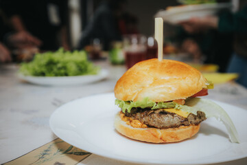 A delicious homemade cheeseburger with lettuce, onion, pickles, tomato, and melted cheddar, served on a soft bun with a wooden skewer on a white plate.