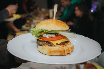 A delicious homemade cheeseburger with lettuce, onion, pickles, tomato, and melted cheddar, served on a soft bun with a wooden skewer on a white plate.