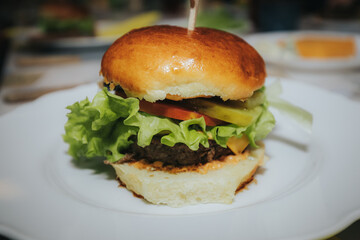 A delicious homemade cheeseburger with lettuce, onion, pickles, tomato, and melted cheddar, served on a soft bun with a wooden skewer on a white plate.