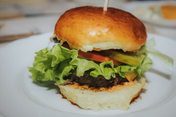 A delicious homemade cheeseburger with lettuce, onion, pickles, tomato, and melted cheddar, served on a soft bun with a wooden skewer on a white plate.