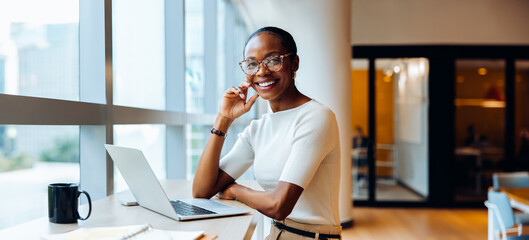 Smiling woman working at desk with laptop and coffee in a bright office