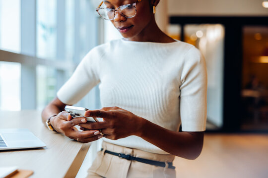 Professional woman using smartphone at desk in bright office setting - Powered by Adobe