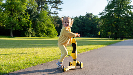 Child scooter riding. Girl yellow scooter park. Motion day lifestyle travel.