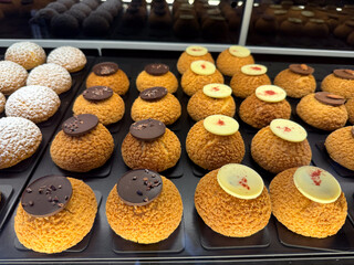 Assorted cream puff desserts with chocolate decoration in bakery display. Indulgence, sweetness and craftsmanship of modern pastry art.