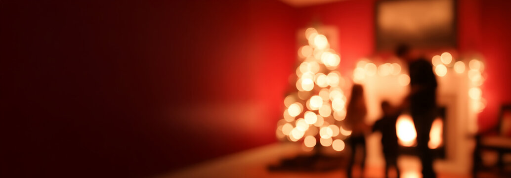 silhouettes d&rsquo;une famille devant une chemin&eacute;e et un sapin de no&euml;l illumin&eacute; sur fond rouge, ambiance chaleureuse blur background avec espace n&eacute;gatif copyspace pour no&euml;l et f&ecirc;tes de fin d&rsquo;ann&eacute;e