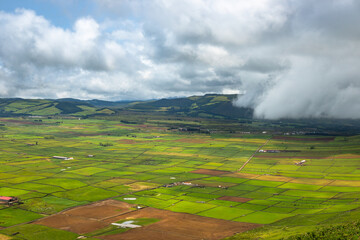 Panoramic view of the colorful agricultural fields from Serra do Cume lookout on Terceira Island, Azores, Portugal. Lush green, yellow, and brown farmlands form a scenic patchwork landscape 