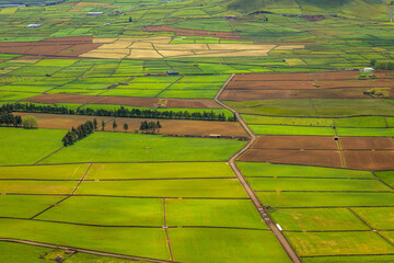 Panoramic view of the colorful agricultural fields from Serra do Cume lookout on Terceira Island, Azores, Portugal. Lush green, yellow, and brown farmlands form a scenic patchwork landscape 