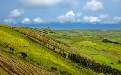 Panoramic view of the colorful agricultural fields from Serra do Cume lookout on Terceira Island, Azores, Portugal. Lush green, yellow, and brown farmlands form a scenic patchwork landscape 