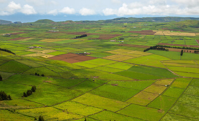 Panoramic view of the colorful agricultural fields from Serra do Cume lookout on Terceira Island, Azores, Portugal. Lush green, yellow, and brown farmlands form a scenic patchwork landscape 